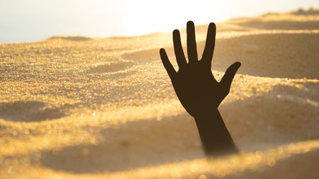 A hand reaches up as if a person has sunk into quicksand.