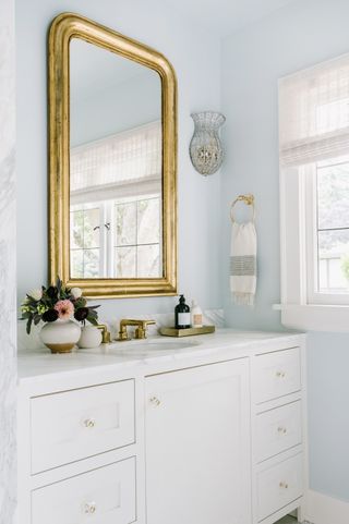 bathroom with light blue walls gold framed mirror and white vanity and worktop