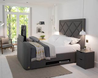A grey modern bed showing a TV displayed in its footboard