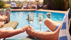 Close up of couple holding hands and champagne glasses with swimming pool in background