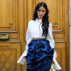 Best perfume oils header image. Woman posing in front of a door wearing a white shirt and blue pants. 