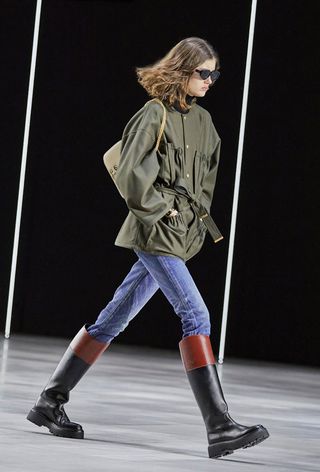 best riding boots shown in a photo from Celine's fall 2022 runway show with a model wearing a green barn jacket with skinny jeans and riding boots