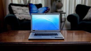 En Acer Chromebook 15 står öppnad på ett träfärgat vardagsrumsbord, med två fotöljer i bakgrunden.
