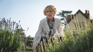 Samantha Bond in a white top as Judith kneels down in some reeds in The Marlow Murder Club.