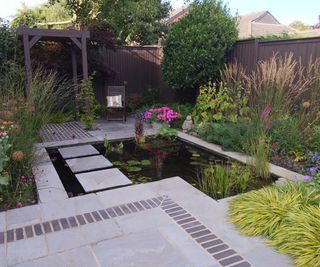 A traditional wooden fence panel around a garden with a water feature and stepping stones