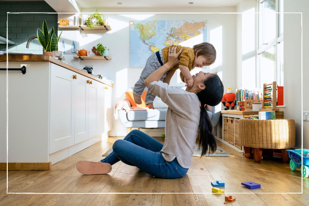 mother holding her child up in the air child sitting on the floor at home surrounded by toys