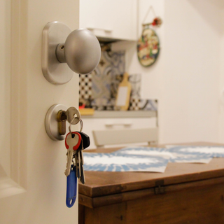 A white front door with a set of keys in the lock. The door is slightly open with an unfocused view of a kitchen behind