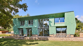 Exterior of a green house with a lawn in front of it and part of a tree in the left hand corner
