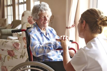 Elderly woman, aged 93, sitting in a wheelchair talking to a nurse in a private retirement home
