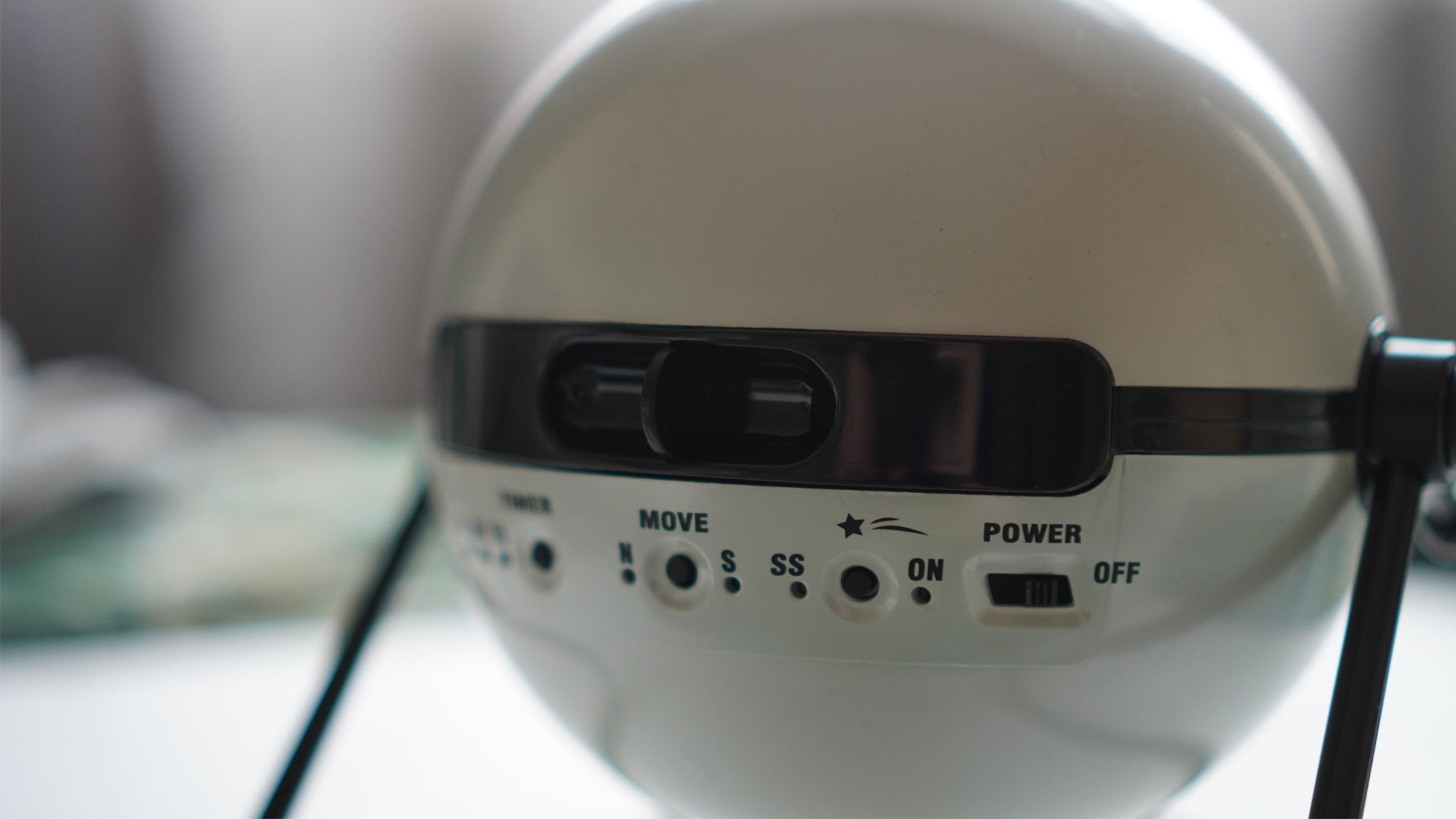 A white sphere sits on a black legged stand on top of a white surface with black buttons on one side of the sphere.