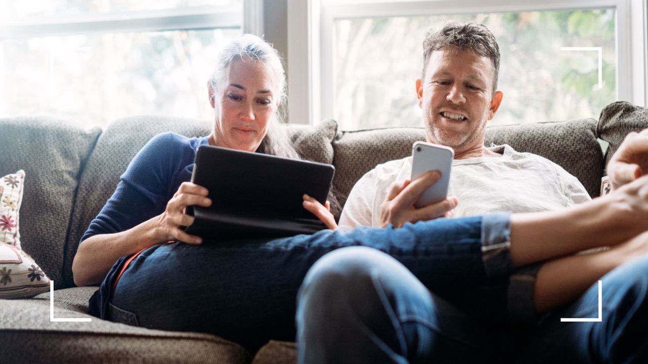 Couple sitting on the sofa together at home looking at digital devices, phone and tablet, to represent phubbing