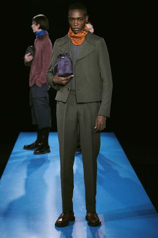 Model wearing grey coat, pant and carried rubberised bag under the arm