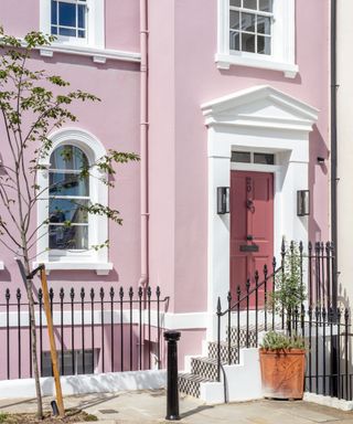 pastel pink house exterior with darker pink front door, black and white check tiles on steps, black painted railings