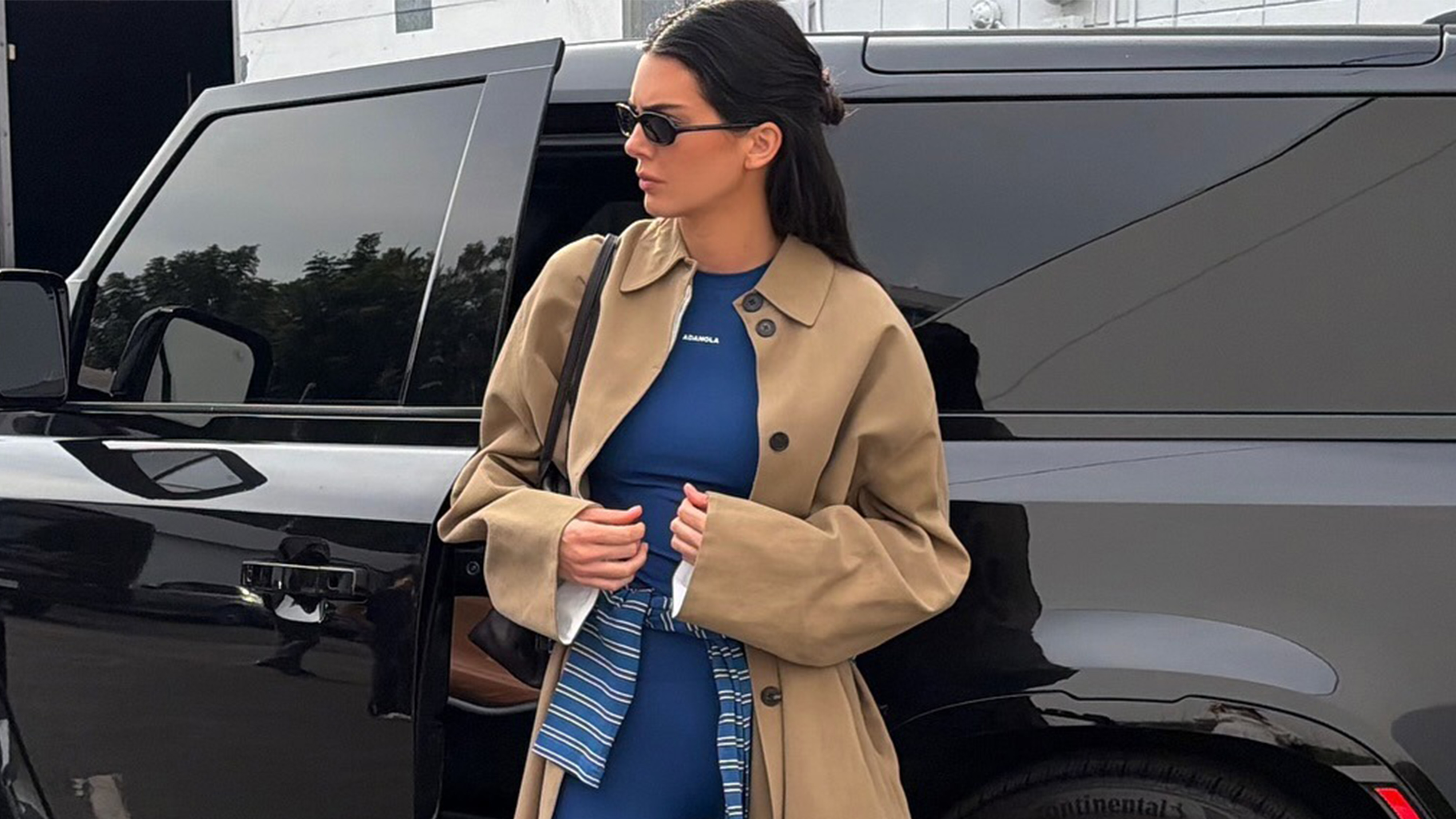 Kendall wears a beige car coat, blue top, blue stripe shirt, and blue leggings.
