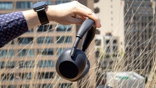 Side view of black Sony WH-1000XM6 noise-cancelling headphones held outdoors in sunshine