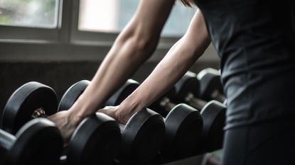 Woman picks up a set of dumbbells from a full rack