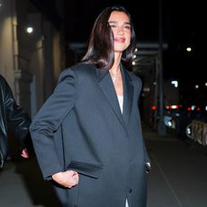 Dua Lipa wearing a black coat, a white dress, and white heels on March 18