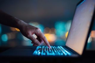 A hand reaching out to press a button on a laptop keyboard