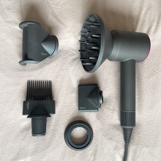 dyson supersonic hair dryer review - Flatlay of the Dyson Supersonic in the Iron & Fuchsia colourway with its attachments