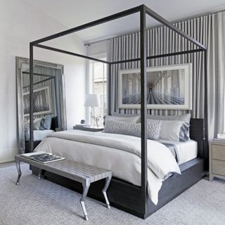 Bedroom with four poster and floorstanding mirror with gray rug and white walls