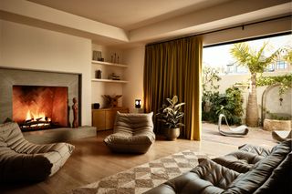 a living room with a lit fireplace, comfy chairs and a jute rug