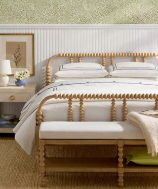 White sheets on a wooden bed frame against white panelled walls with sage green wallpaper.