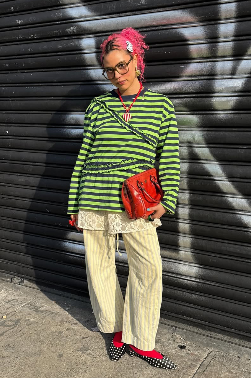 a woman wearing a green and black long sleeve shirt, white striped pants, red socks, and black-and-white polka dot shoes