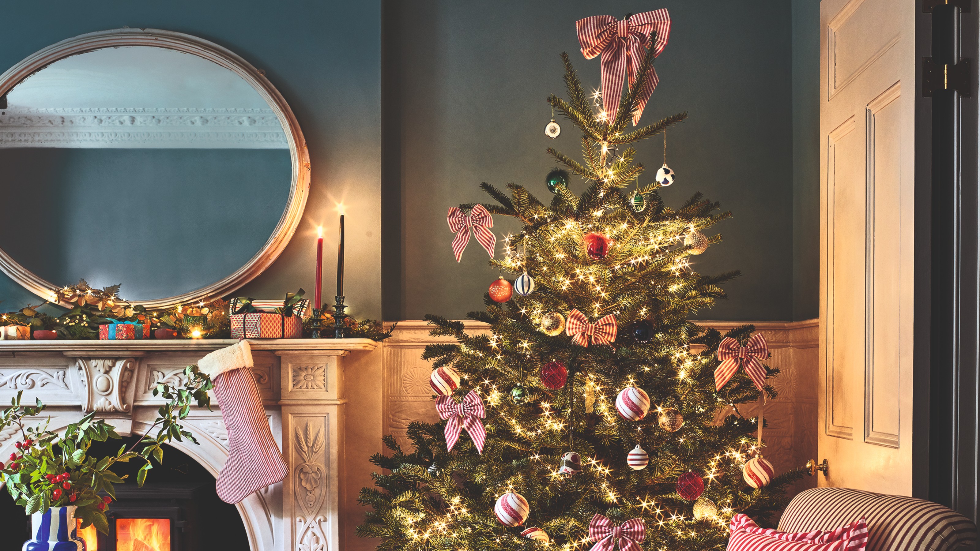 A living room decorated for Christmas with a lit-up tree and a garland with Christmas lights on the mantelpiece