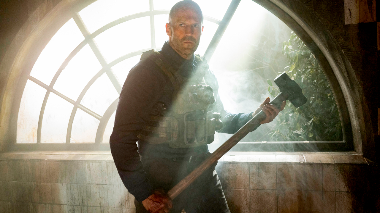 Jason Statham poses with a sledgehammer in front of a very bright window in A Working Man.