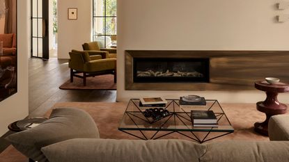 Image of a white living room with a red side table and a pink rug. There is a metal fire place and a silver side table by the large gray sofa.