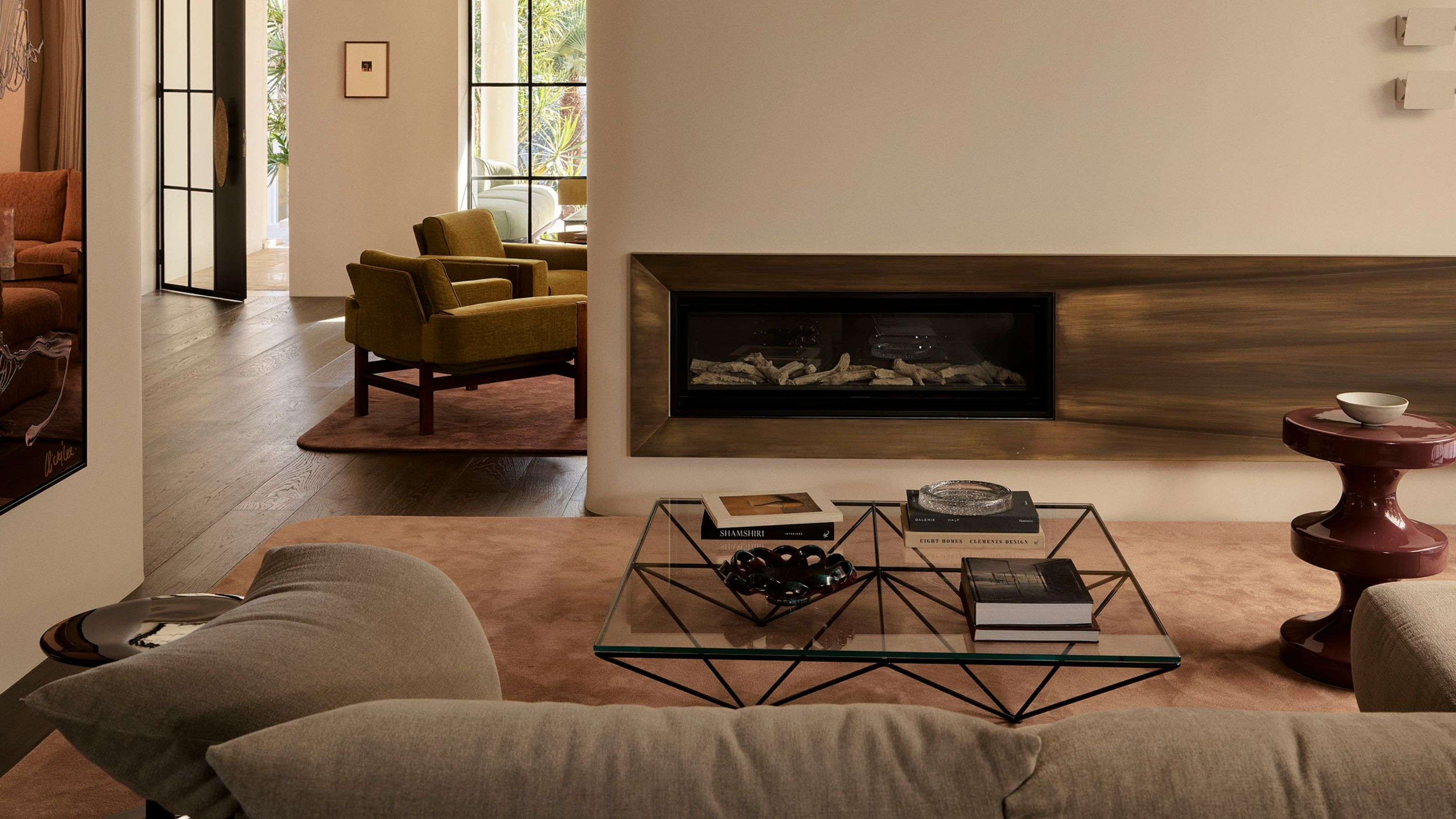 Image of a white living room with a red side table and a pink rug. There is a metal fire place and a silver side table by the large gray sofa.