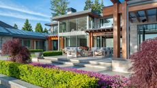 A large backyard and patio with patio furniture and plants around the borders of the garden. There is a view of the outside of a home that has large windows 