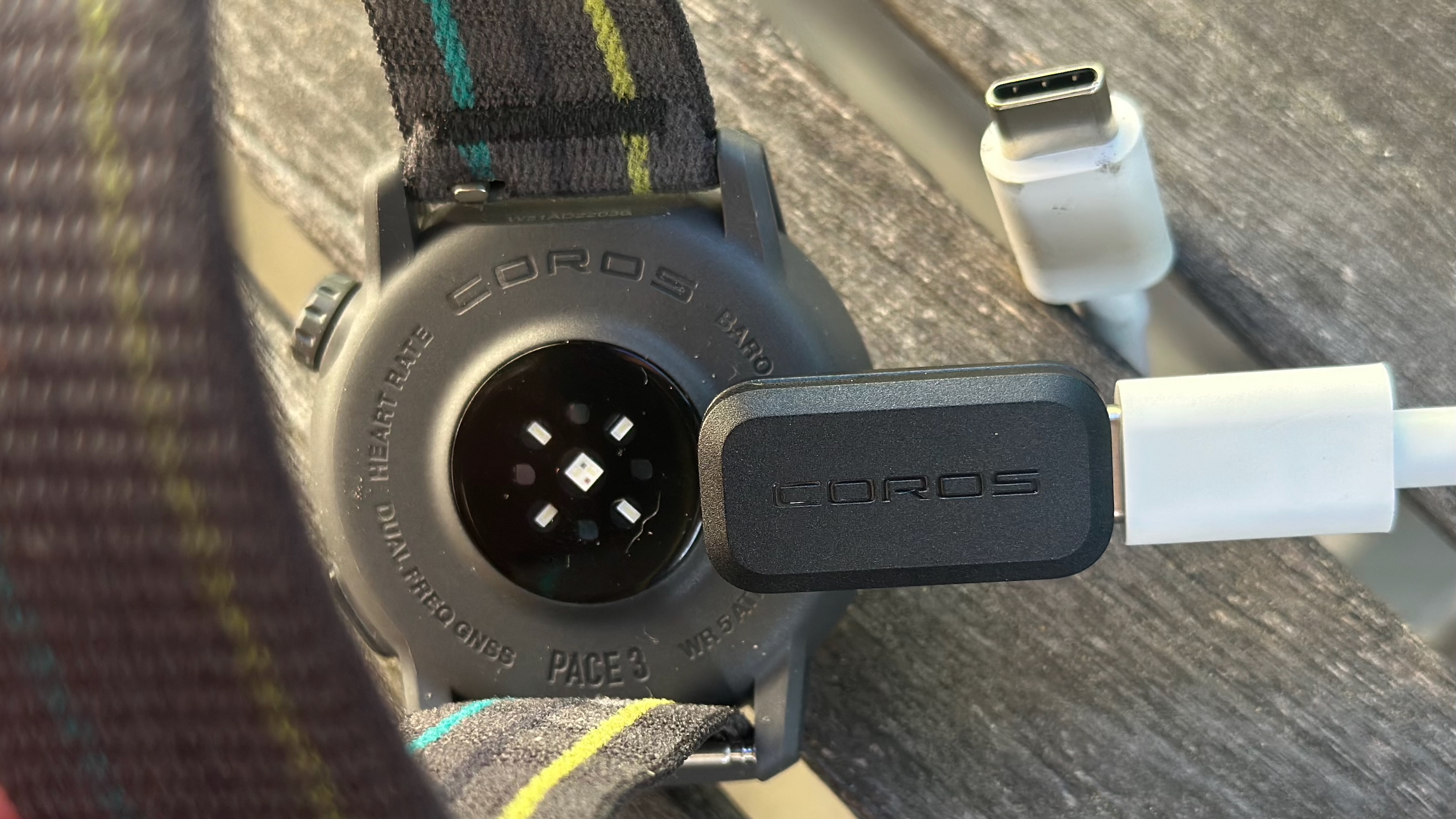 The USB-C to COROS A1 Charging Adapter with a USB-C cable plugged into it, plugged into a COROS PACE 3 smartwatch.