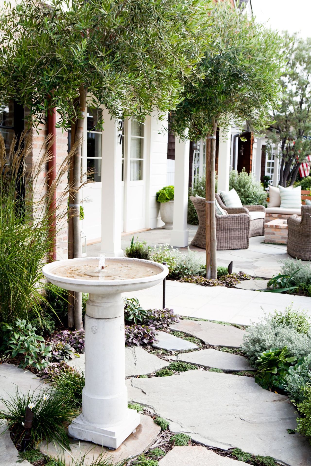 white house exterior with light stones edged with various low growing plants and a water feature