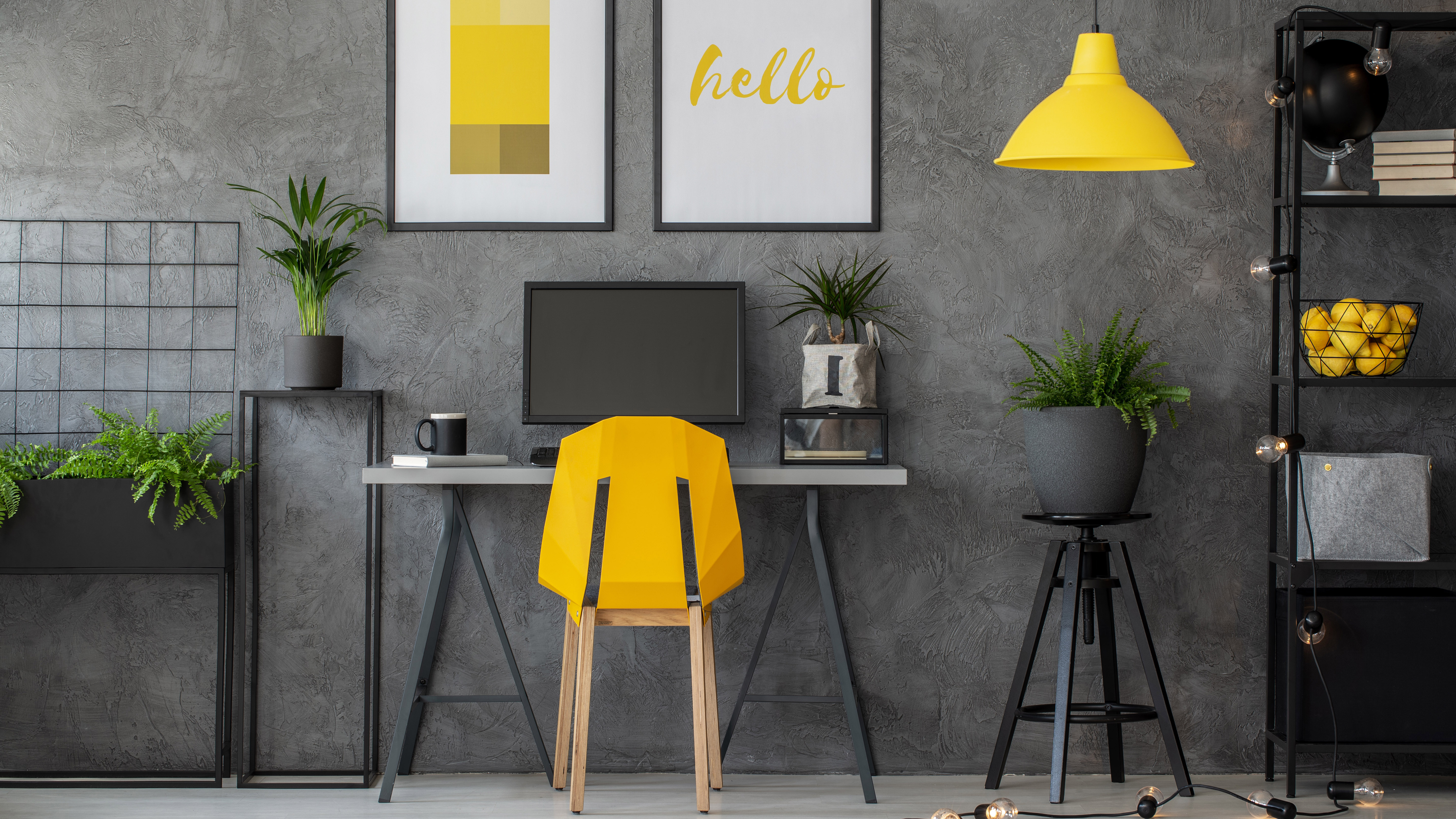 A dark grey themed home office with a yellow chair, lamp and lemons to decorate