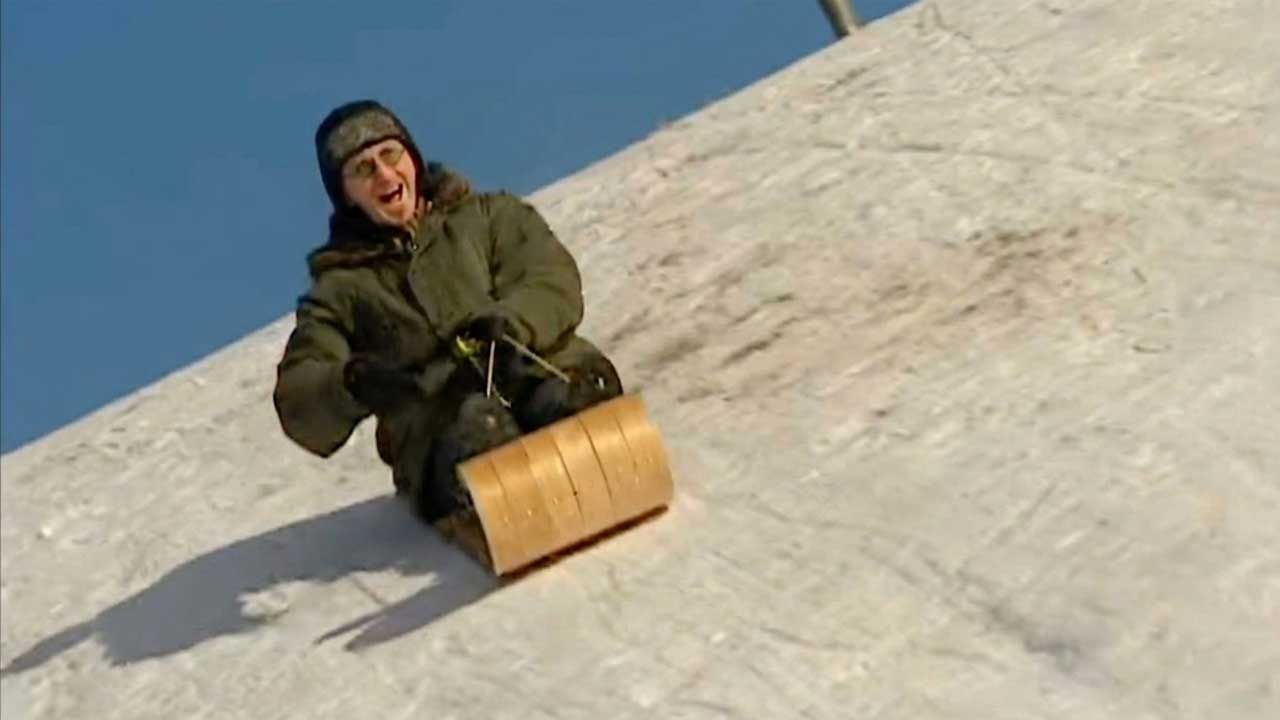 Geddy Lee racing downhill on a toboggan