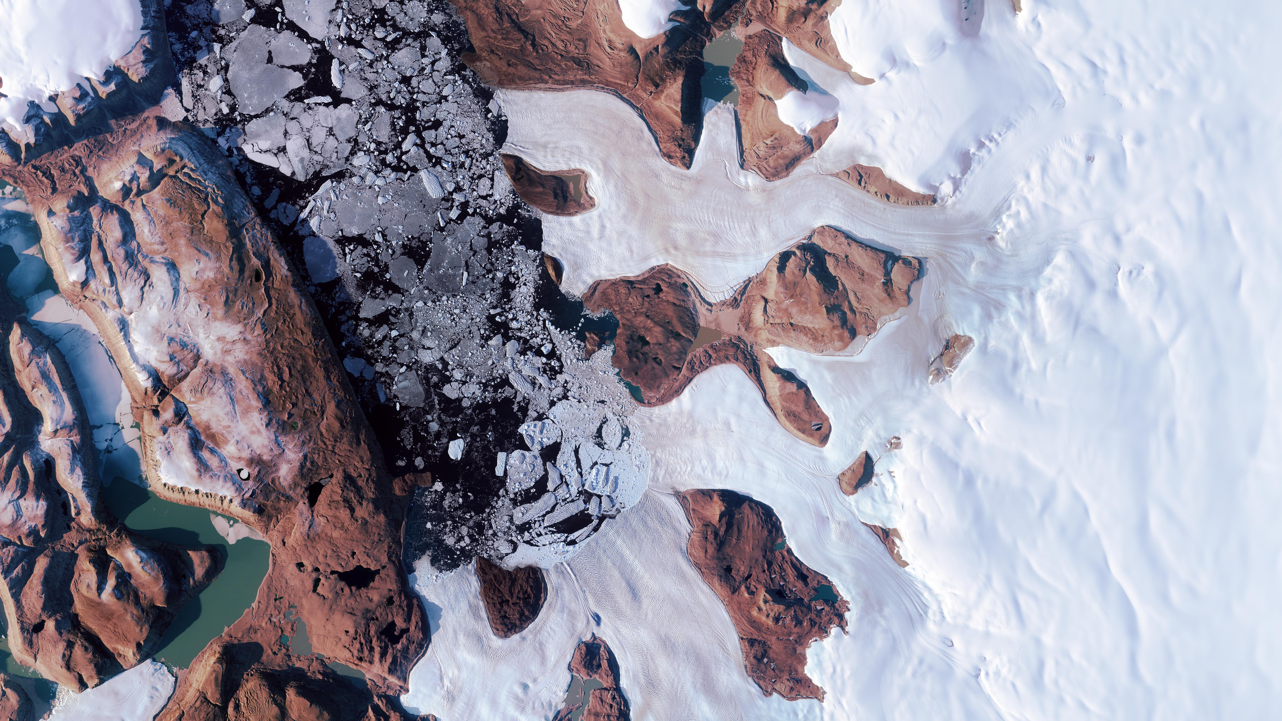 An aerial view of a snowy sheet toward the right and rocky areas toward the left. There appears to be a stream within, very close to the left side.