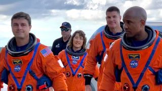 four humans walking on Earth with orange spacesuits. another background human wears black.