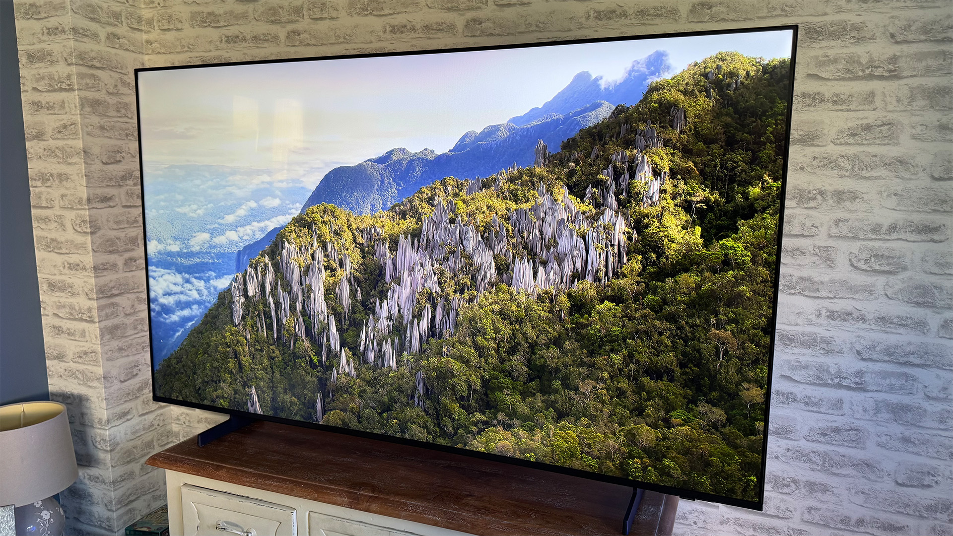 Samsung UE65U8000F 65-inch TV on wooden sideboard in front of brick wall, on screen is mountain range