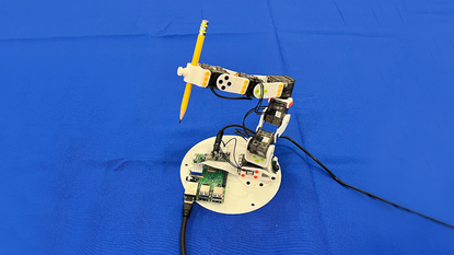A soft robotic hand curls its fingers to grasp a wooden pencil.