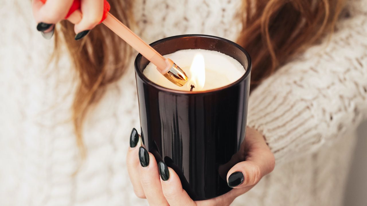 A woman with long hair, whose face you can&#039;t see, in a white sweater with black nail polish lighting a candle with a lighter