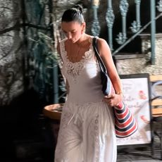 Dua Lipa walks down the street wearing bloomer trousers with a white lace-trim tank top.