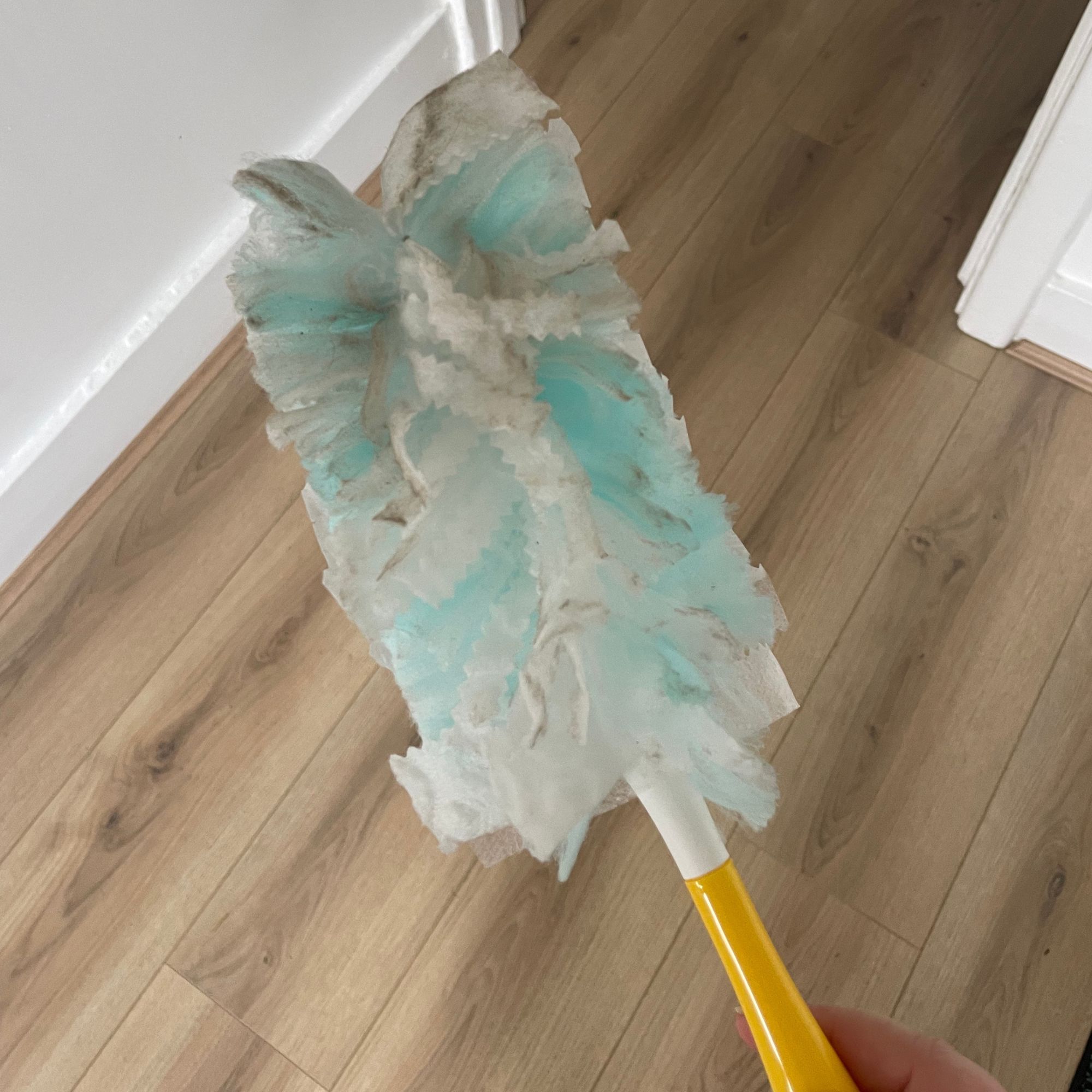 Hand holding Flash Dust Magnet feather duster above wood-effect flooring