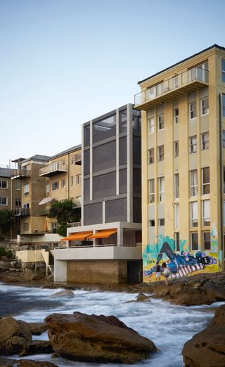 An image with multiple high rise residential buildings by the rocky shores. One of the building has grafitti.