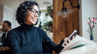 Woman typing on phone, sitting down in cafe wearing glasses and smiling