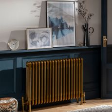 A brass painted radiator against blue painted panelled wall