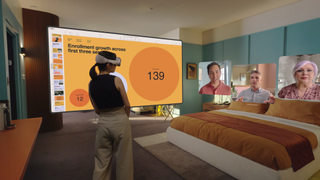 A person wearing a Vision Pro headset in their bedroom, with a large virtual image of a slideshow to their left and ahead of them three panels displaying life-size video feeds of colleagues.
