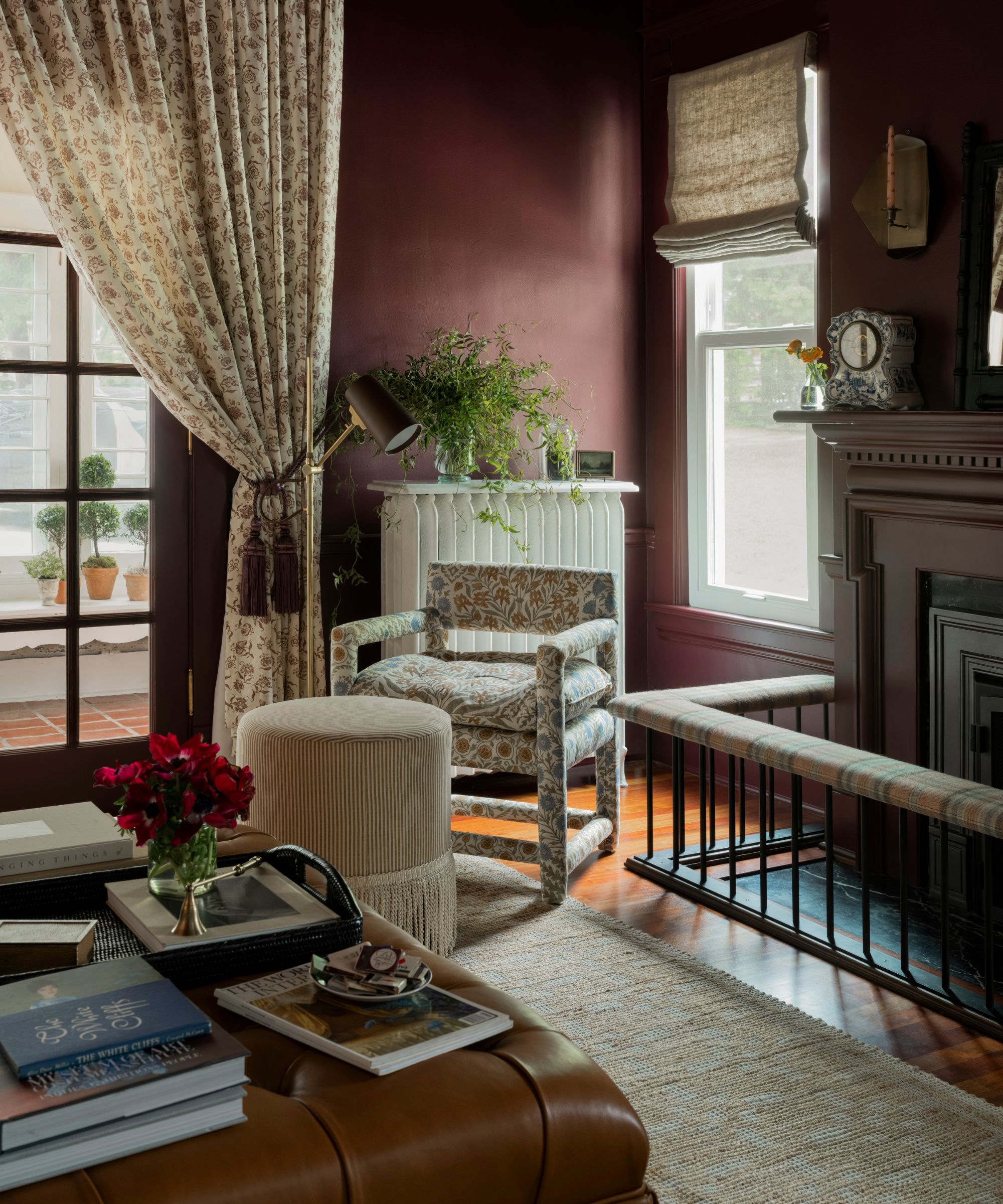 dark purple color drenched living room dressed with a light blue couch, leather ottoman, floral armchairs and drapes