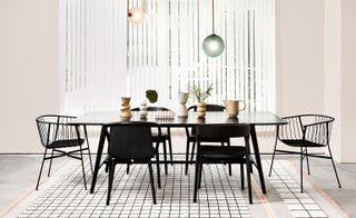 A black dining table with matching chairs stands on a white rug with a black line cube pattern.