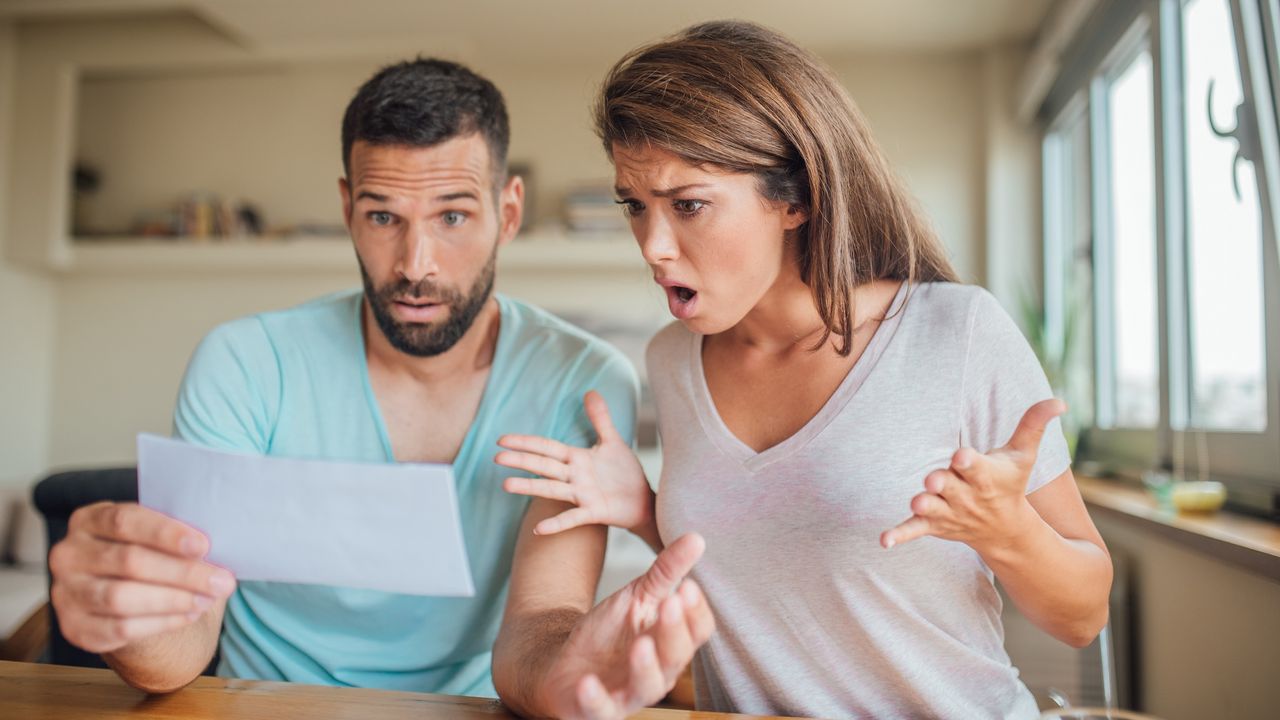 A couple look surprised as they look at a bill together.